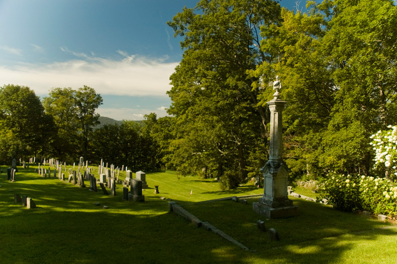 An urn on a pillar, tombstones in a green field, and blue sky.