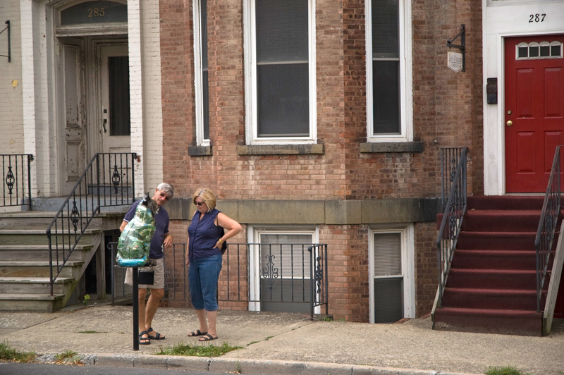 Two people admire a brightly painted cat sculpture on a post.