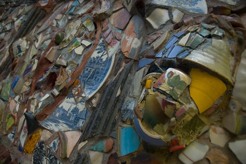 Bits and pieces of broken pottery form a face and background on a wall.