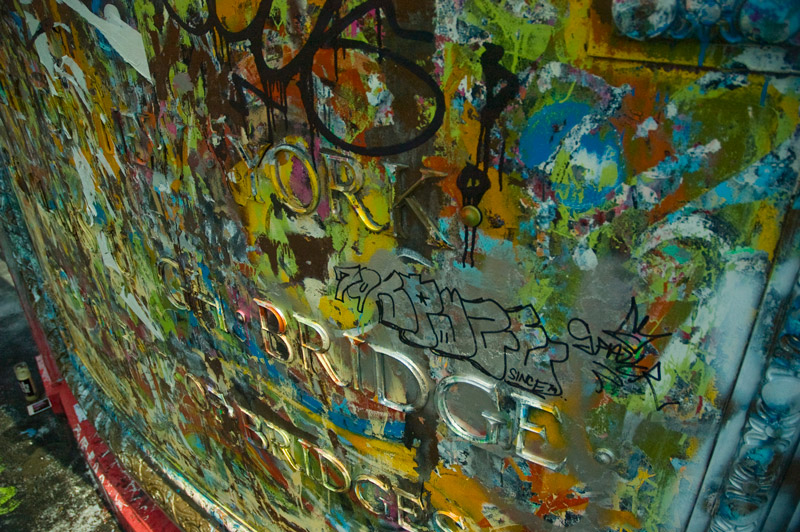 A bridge's name plaque has been covered by colored splotches from many graffiti artists.