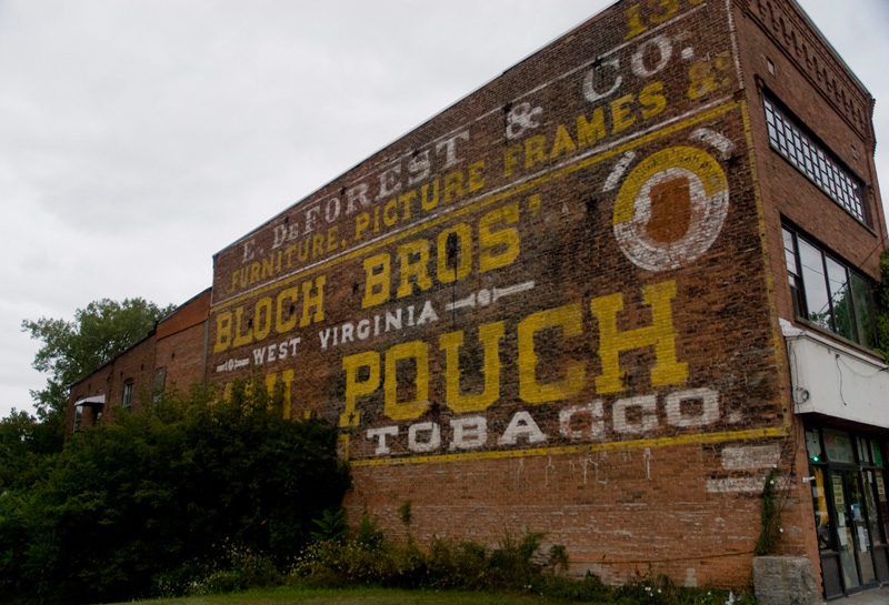 A large building wall, covered with an old sign for tobacco.
