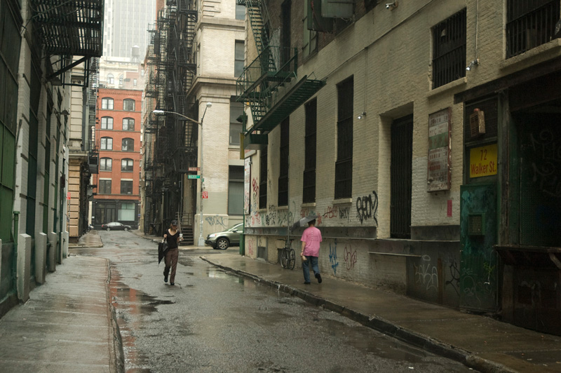 Pedestrians passing each other in a wet alley with puddles.