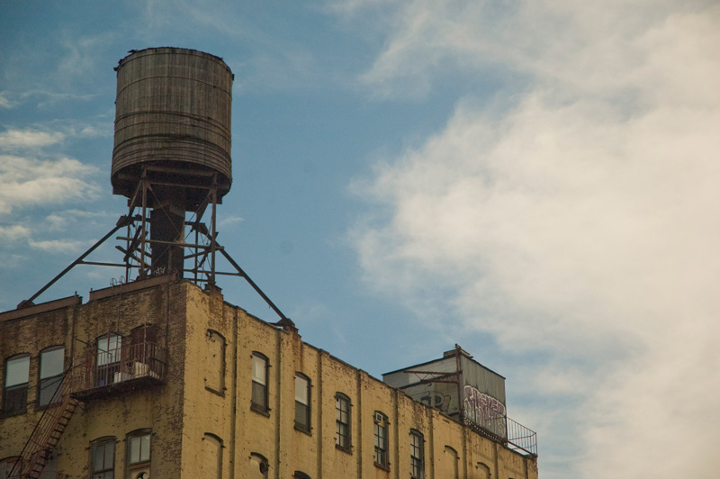 An old wooden water tank, perched on an apartment building; blue skies.