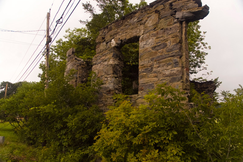 Remnant of a stone-work wall, with a window, surrounded by brush.