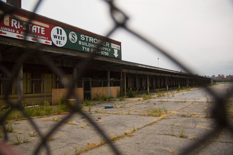 Behind a fence, a parking lot with weeds, and a series of parking ports.