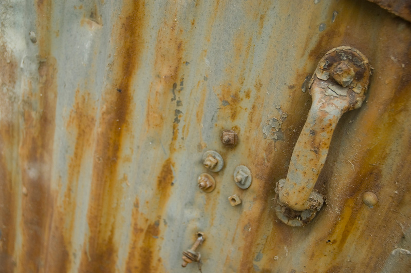 A metal door and handle, with streaks of rust and peeling paint.