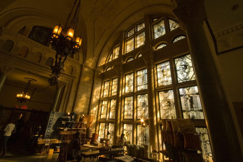 Sunlight streams through a high, arched window, onto a seller's goods.