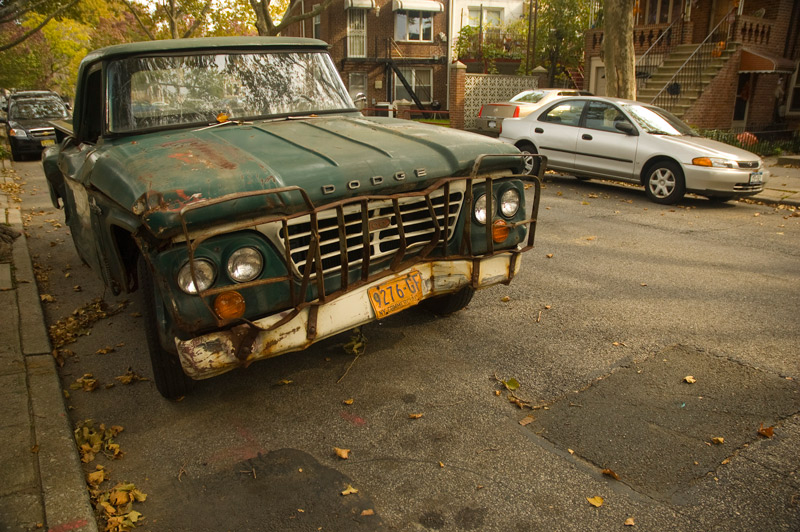 The front end of a green truck, on a street with trees in autumn colors.