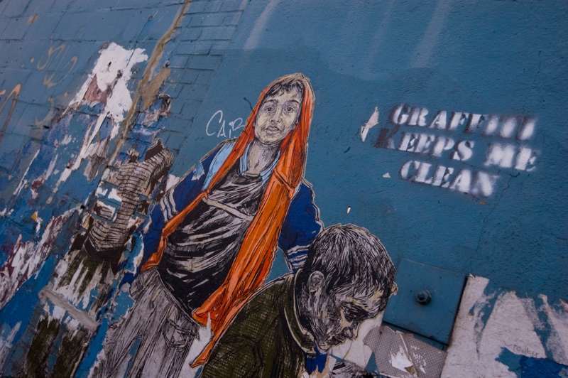 A blue wall with wheat paste street art and a stenciled message.