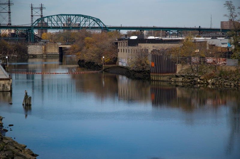 A steel overpass, a blue river, and industrial buildings.