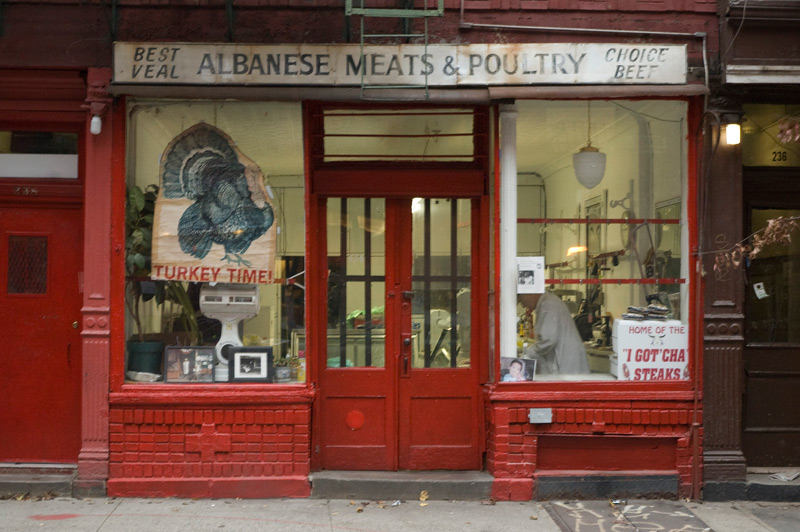 A butcher's storefront, with window advertisements and the butcher behind the window.