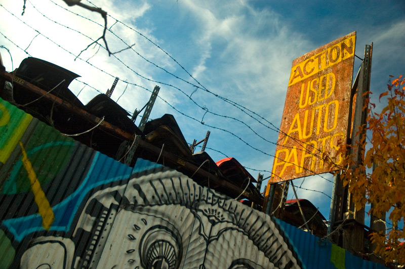 An auto parts dealer's old sign, above a corrugated metal fence.