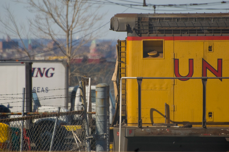 Part of a rail car, behind chain link fence.