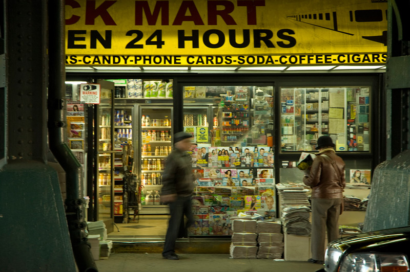 A deli, under a dark overpass, with customers reading newspapers.