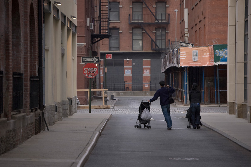 A mom and dad head down an alley, each pushing a stroller.