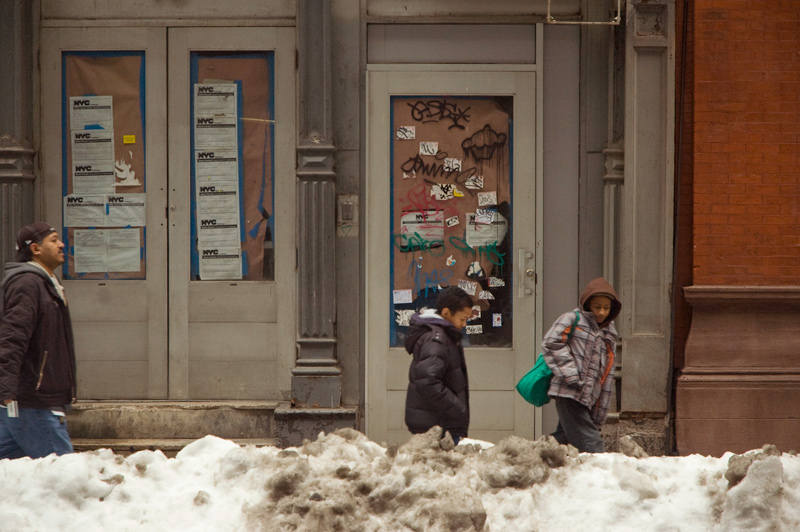 Pedestrians walk behind piles of plowed, dirty snow.