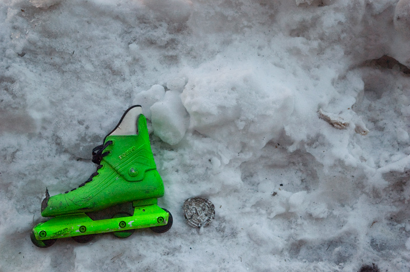 One green roller skate, lying in dirty snow.