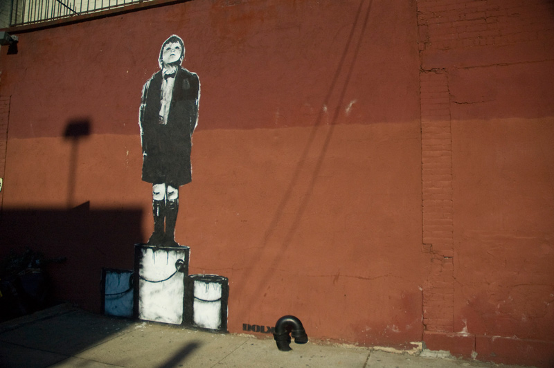 Street art showing a boy standing on cans and peering far.