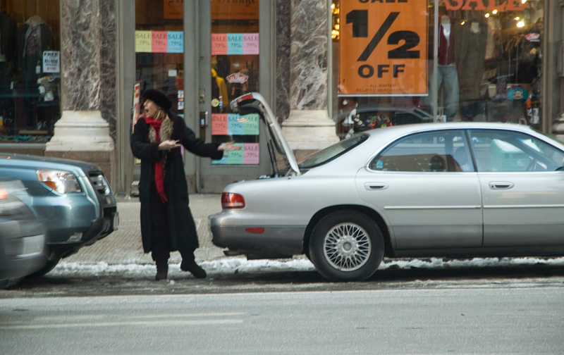 A woman at a car screams in frustration about the car to others on the street.