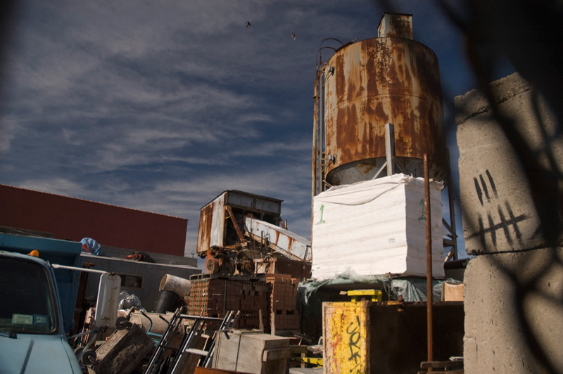 Raw materials and rusting metal tanks and chutes in a factory yard.