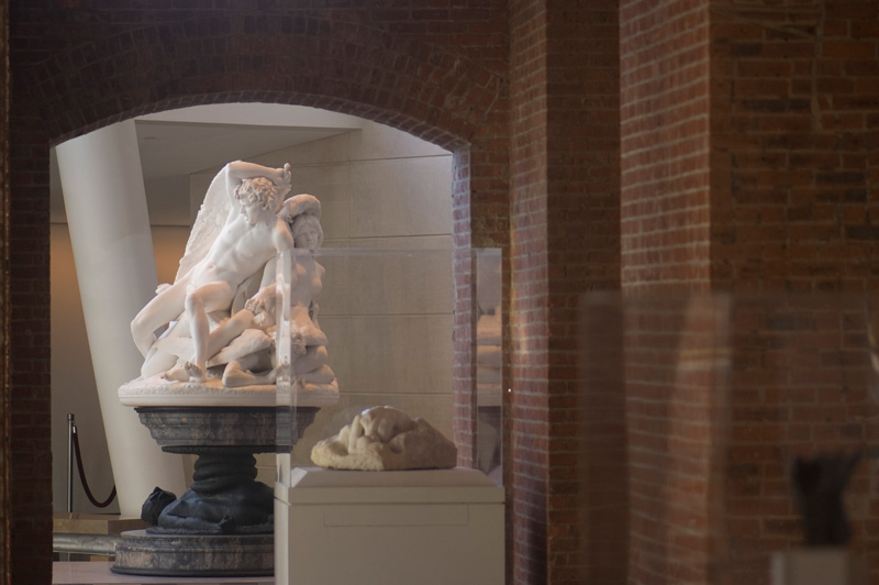 A white sculpture on a pedestal, under a walkway.