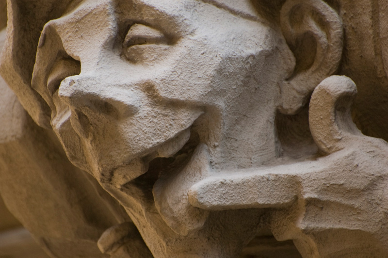A smiling face, licking his finger, carved from stone.