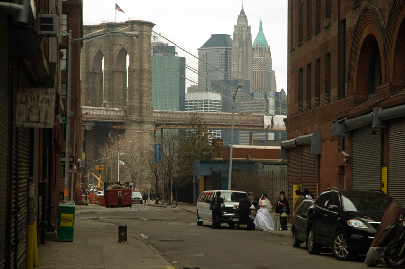 A wedding party exits a limo by the Brooklyn Bridge.