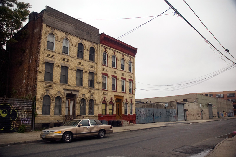 A dented cadillac in front of an isolated apartment building.