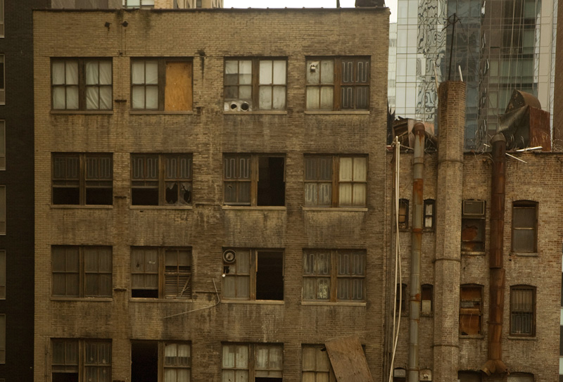 Boarded up windows and sooty chutes on a building.