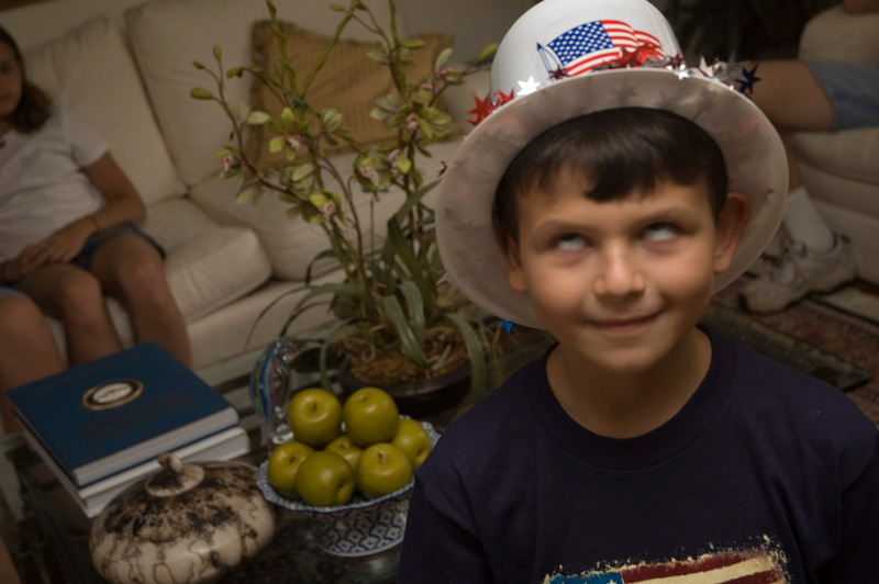 A boy rolls his eyes, wearing a plastic hat with a flag on it.