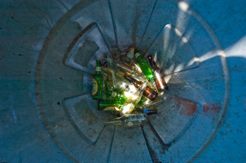 A variety of beer bottles at the bottom of a trash can.