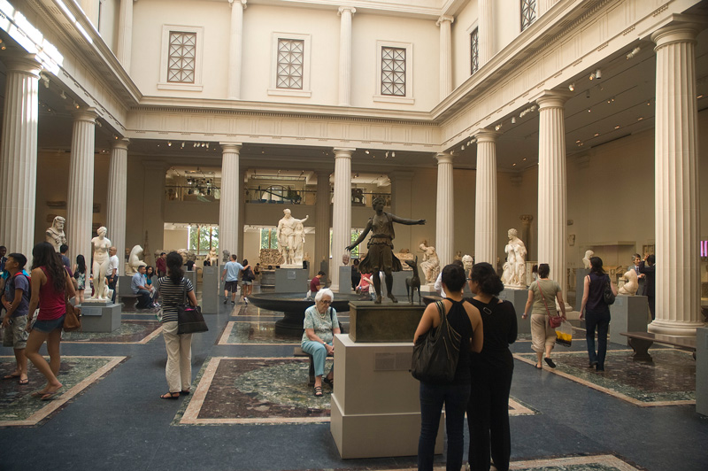 An older woman finds respite in a bench in a sculpture gallery.