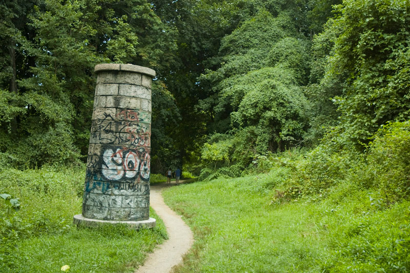 A stone cylinder on a path among greenry.