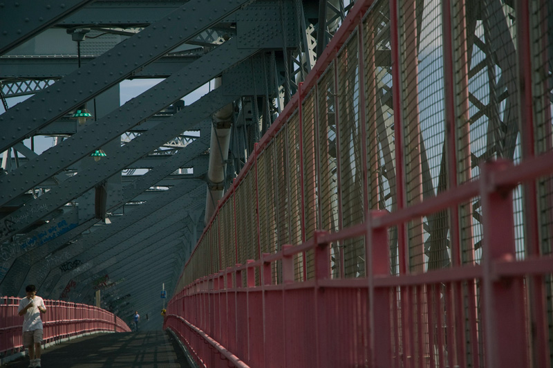 A person walking past the hump of a steel lattice bridge.