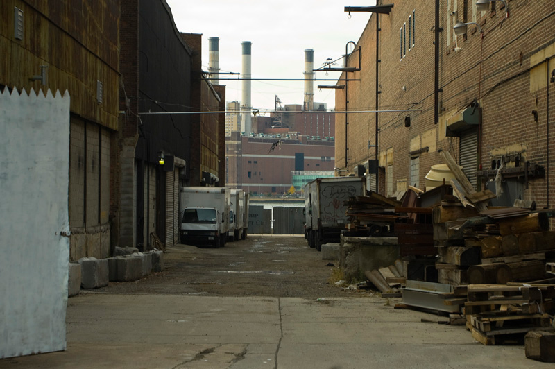 smokestacks, trucks, and crates in an alley.