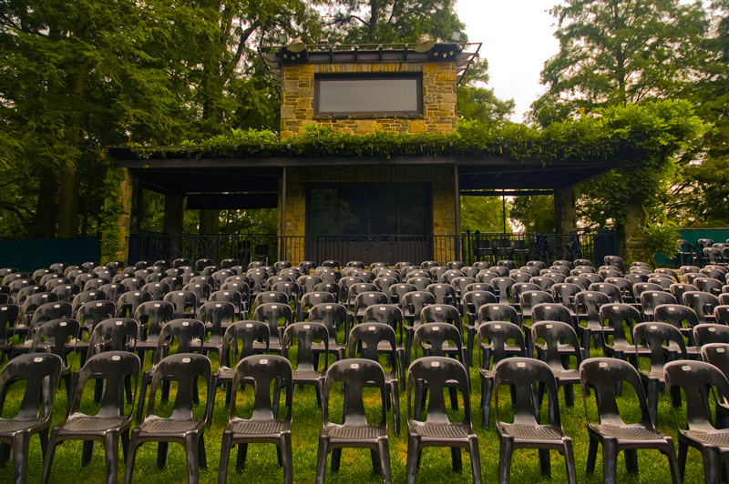Rows of empty black chairs, in an outdoor setting.