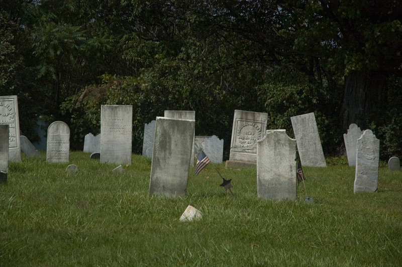 Old tombstones in a small graveyard, one decorated with an American flag