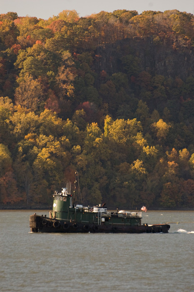 A large tugboat, with trees in autumn colors.