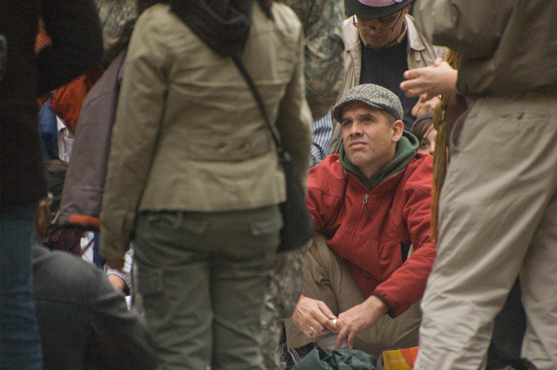 A man sitting in a crowd listens to someone nearby.