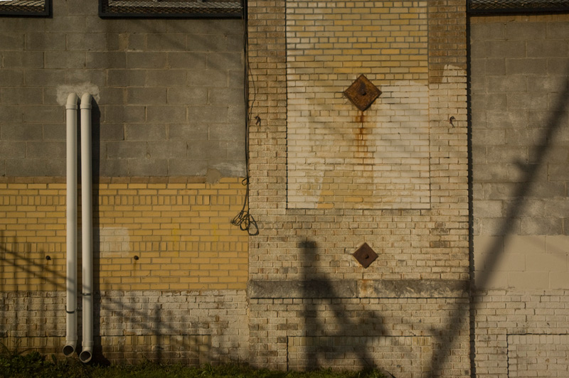 A brick wall, with rusting pipes and shadows.