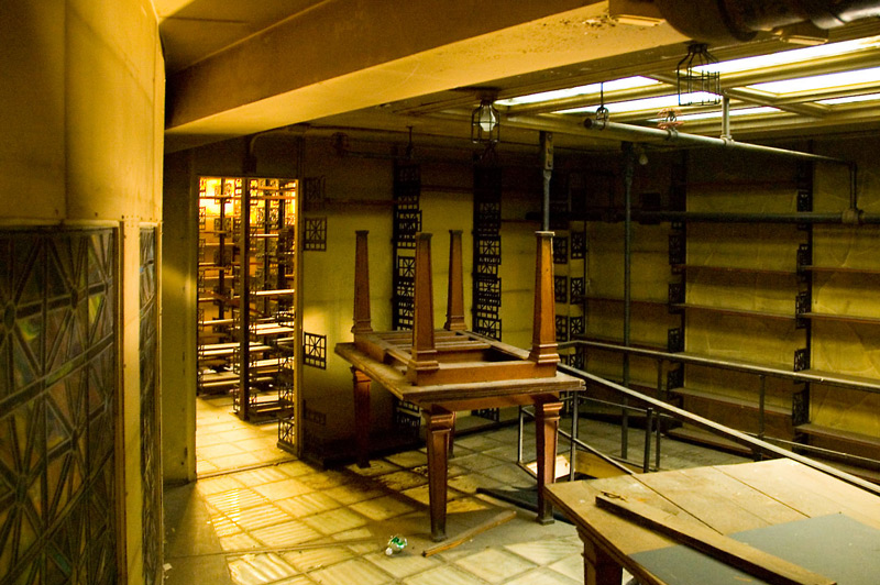 A dusty room with wooden tables stacked on one another.