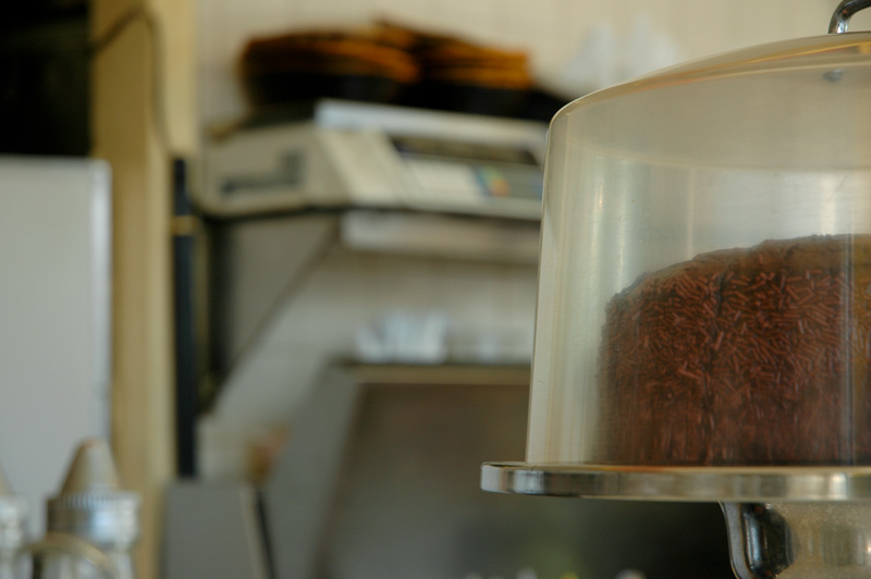 A chcocolate cake under glass, on a diner counter.