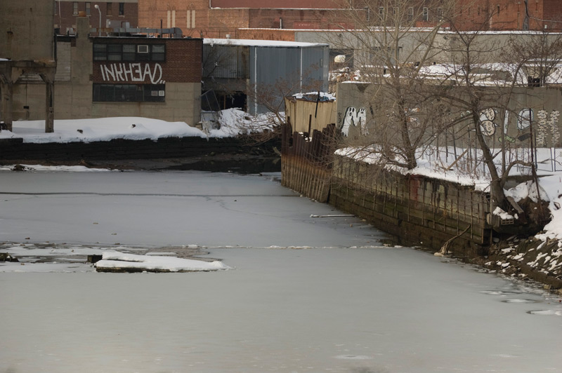 A frozen canal, by industrial buildings.