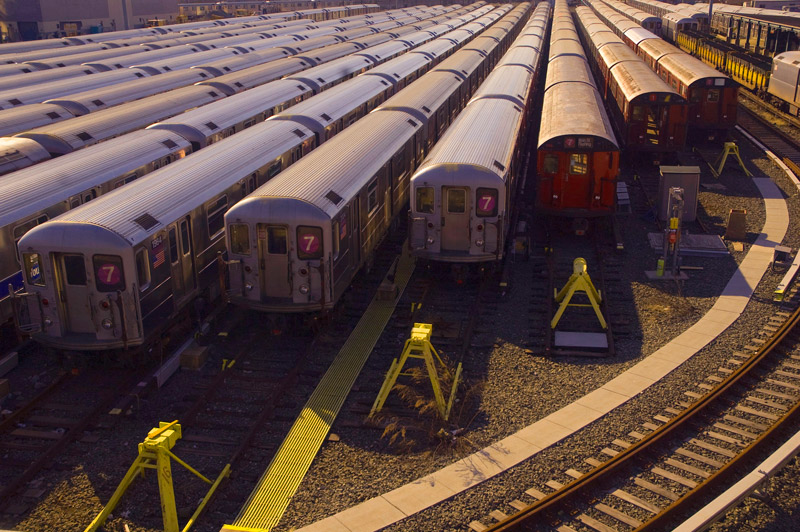 A dozen trains sitting in the afternoon sun, in a train yard.