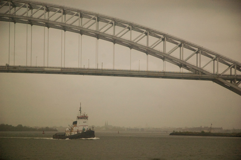 A tugboat passing under a steel bridge