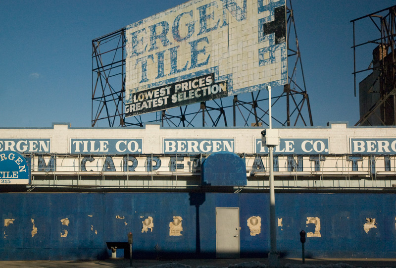 Blue and white signage on a tile store, boarded up with blue plywood