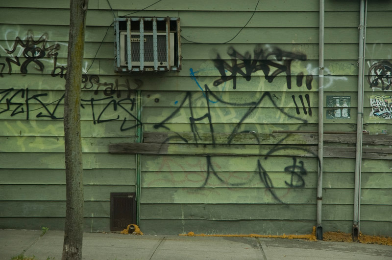 A green wall, with graffiti and a protruding air conditioner