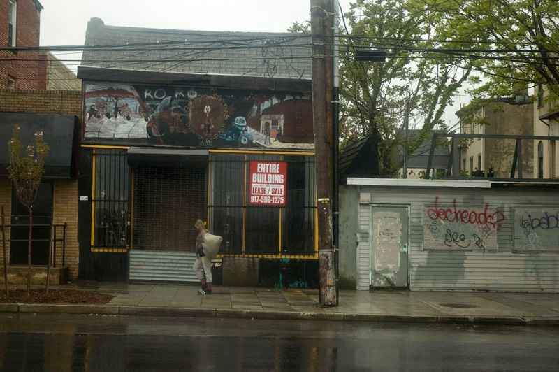 A pedestrian passing an abandoned building where it has rained