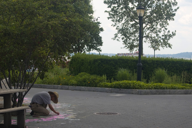 A man drawing a floral design on a sidewalk, with pink chalk