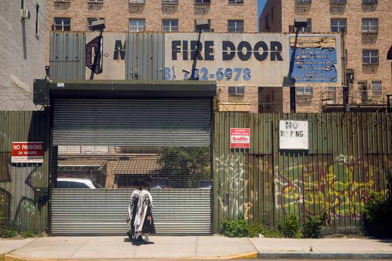 Two Hasidic Jews walk past a parking lot with outdated signs